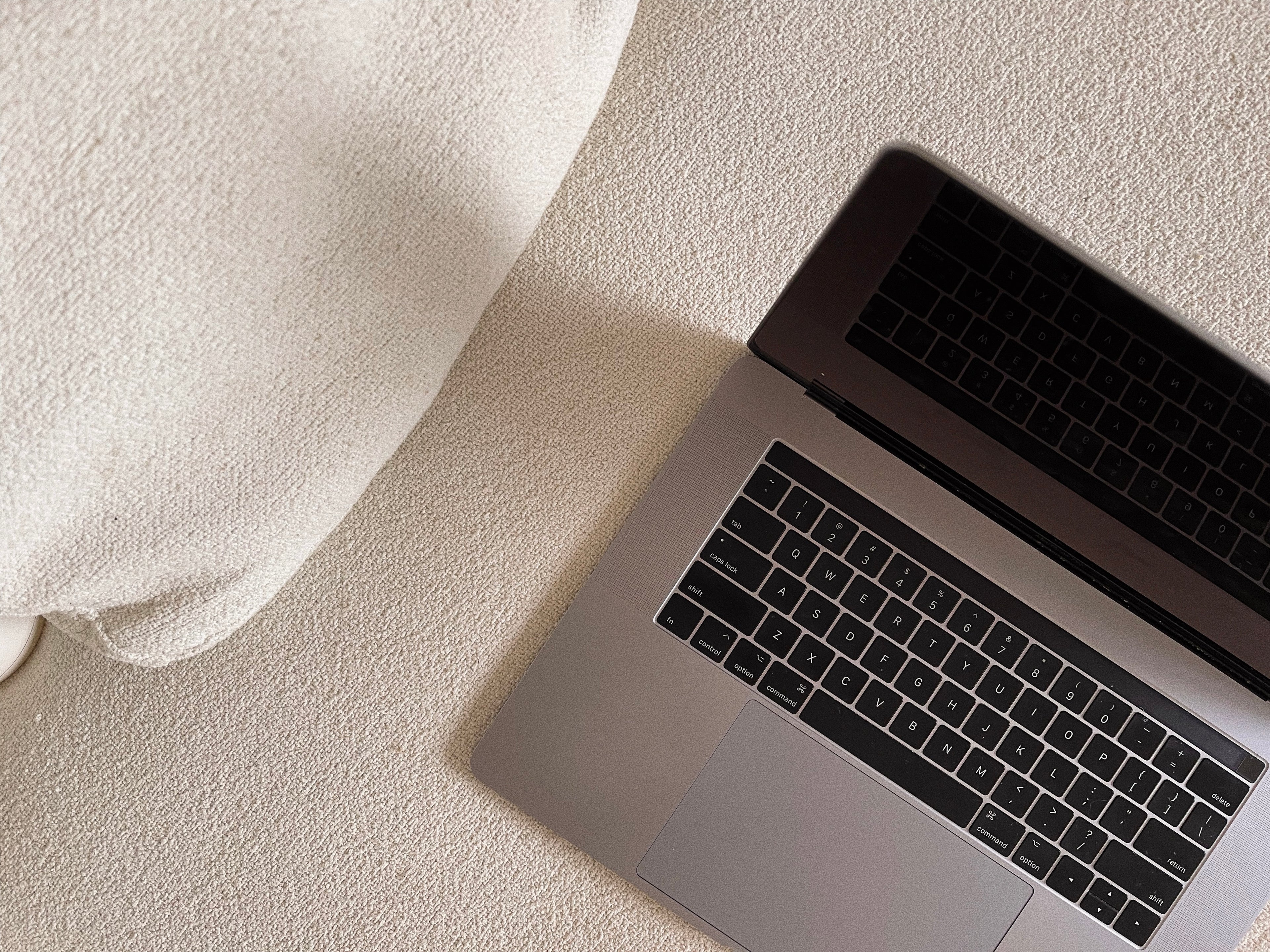 Silver MacBook on cream textured surface beside white knit fabric, overhead view